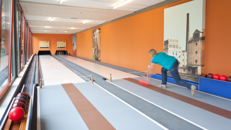 Bowling alleys, © JUFA Person bowling on a bowling alley with an orange wall.