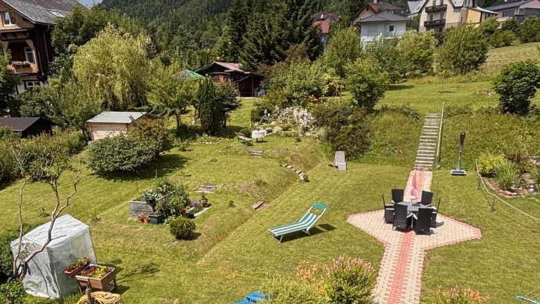 Garden, © Familie Mohr A well-tended garden with a lawn, garden furniture and a cobblestone path. Houses and wooded hills can be seen in the background.