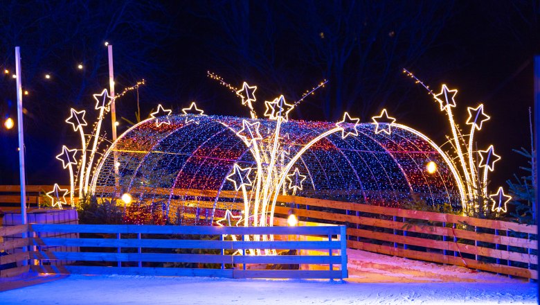 Ice skating rink in the Eis-Greissler Welt, © Blochberger Eisproduktion GmbH Illuminated ice rink with stars and tunnel of lights at night.