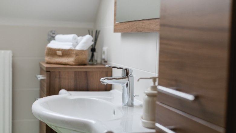 Bathroom with shower, © heiter-weiter.at/Karl Stangl Modern bathroom with washbasin, wooden cabinets and towels in a basket.