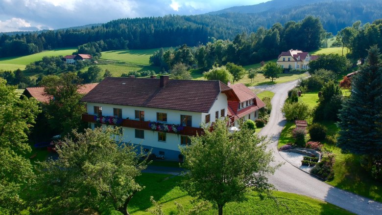 ...surrounded by nature., © Familie Rosinger Rural landscape with a large house, surrounded by trees and meadows, under a cloudy sky.