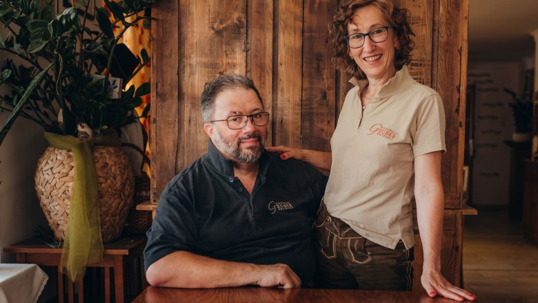 Innkeepers Andrea and Johann Gruber, © Niederösterreich Werbung/Daniela Führer Two people in a rustic room, one sitting, the other standing with a smile.