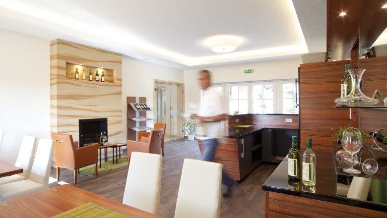 Tasting room, © Astrid Bartl A modern tasting room with wooden furniture, bottles of wine and a blurred man in the foreground.