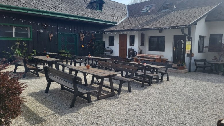 Leo-Hof guest garden, © Leo-Hof/Sandra Reinisch A guest garden with wooden benches and tables on gravel in front of a traditional building.