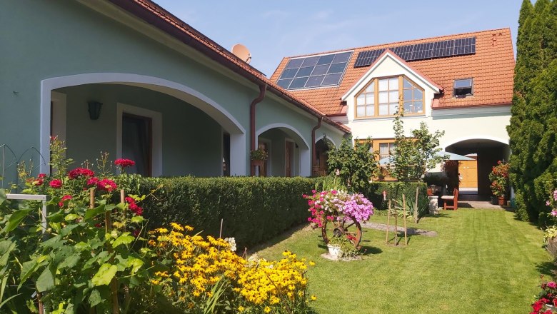 20210813_152903_garten_mittel, © Schwarzinger A well-tended garden with colorful flowers and a house with solar panels on the roof.