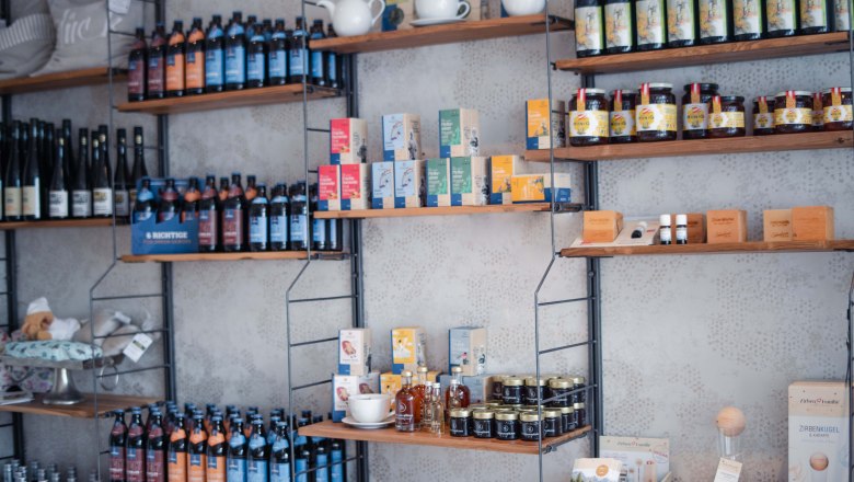 Product selection in the Taflerei store, © Hotel Schachner_MIKU Media Shelves with various products such as bottles, tea packs and honey jars in a store.