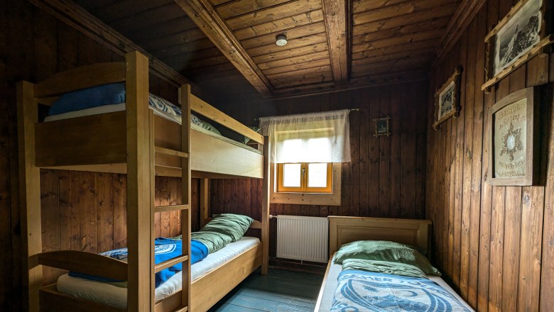 Karl-Ludwig-Haus - Triple room, © Kai Weidinger Wood-paneled triple room with bunk bed and single bed, window with curtain, rustic furnishings.