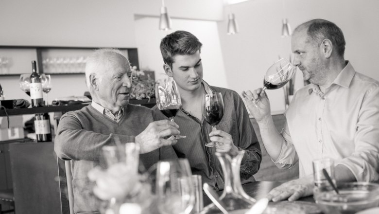 Three generations, © Astrid Bartl Three men clink glasses of wine at a table.