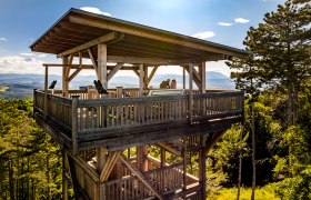 The Lanzenkirchen-Wiesen lookout point, © Wiener Alpen, Fülöp, Kremsl Wooden observation tower in the forest with two people on the platform.