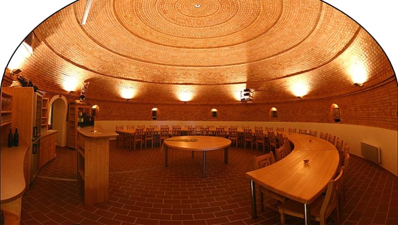 Wine dome, © Winzerhof Scheit Interior view of a round wine cellar with brick walls and wooden furniture.