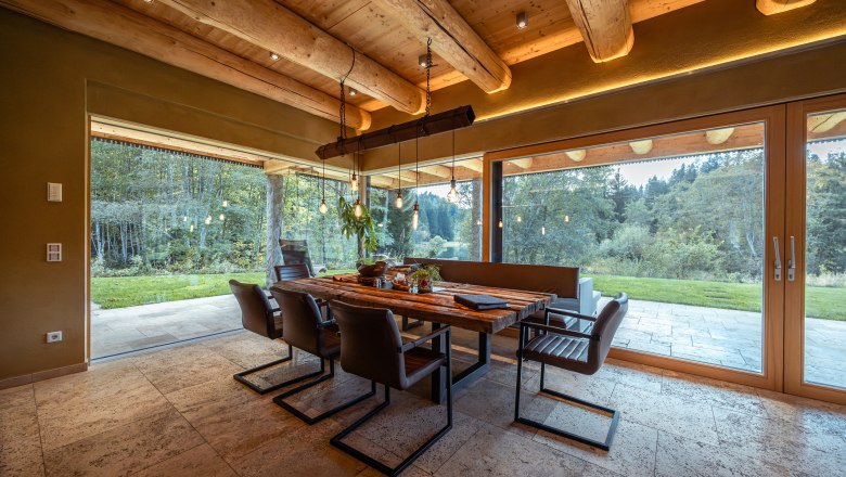 Vacation home by the lake, © Niederösterreich Werbung / Maximilian Pawlikowsky Interior view of a modern dining room with wooden beamed ceiling and large window overlooking a garden.