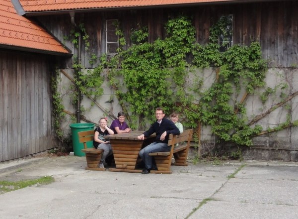 Weißensteiner organic farm, © Wolfgang Weißensteiner Four people sit at a wooden table in front of a building overgrown with ivy.