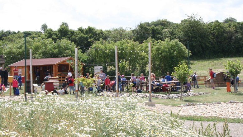 Schrattenberg, © Helmut Kaufmann People sit at tables outside, surrounded by flowers and trees.