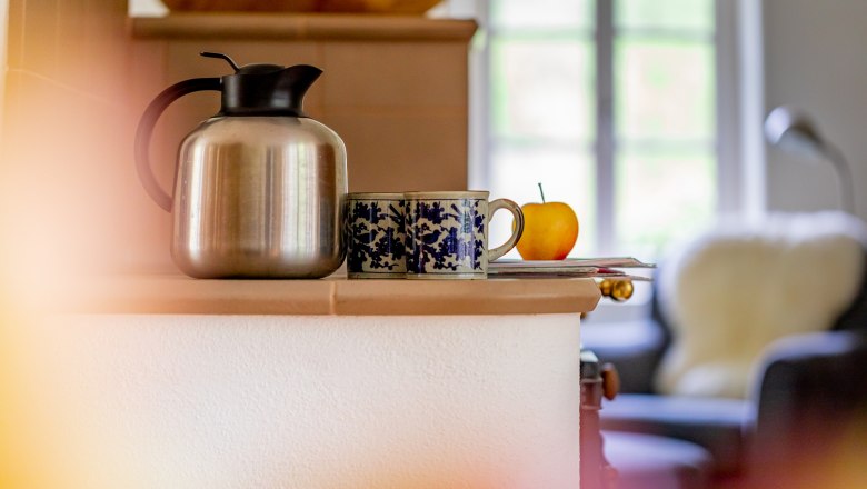 Cavalier houses, © Wiener Alpen / Christian Kremsl A table with a thermos flask, two cups and an apple in front of a window.