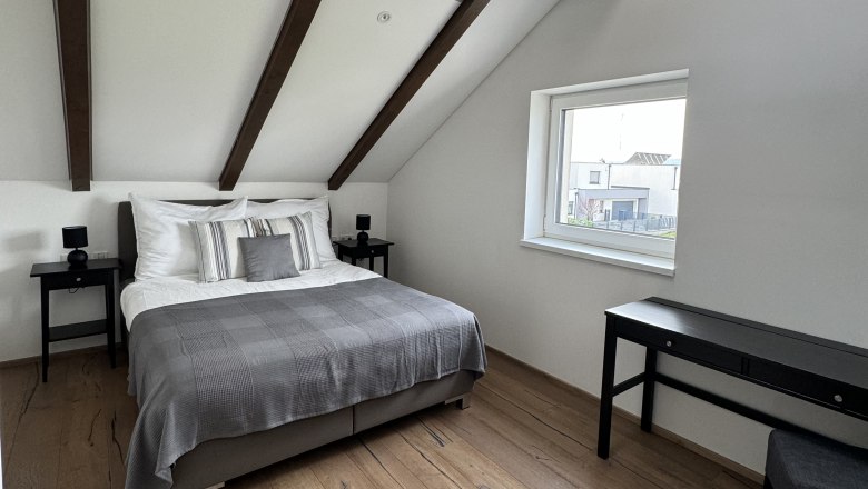 Bedroom, © Juwel am Stadtrand Modern bedroom with wooden beamed ceiling, double bed, wooden floor and window.