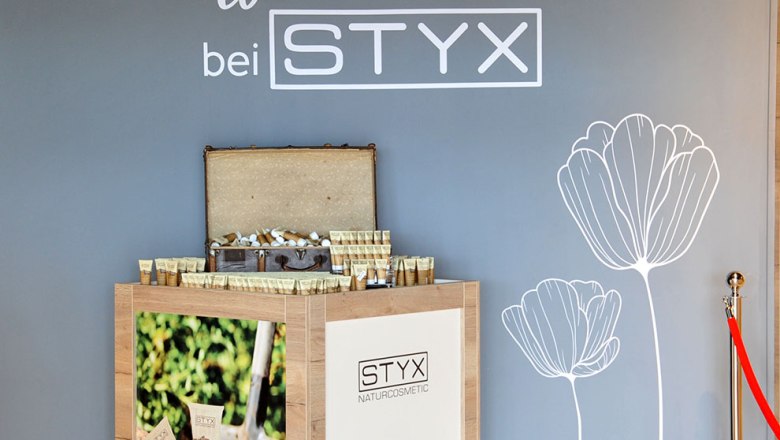 STYX Welcome Center- Shop, © Styx Naturkosmetic GmbH A display with STYX natural cosmetic products in front of a gray wall with a flower drawing and a welcome greeting.