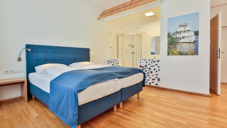 Hotel Unter den Linden Room 204, © Hotel Unter den Linden Hotel room with blue bed, wooden floor and open shower.