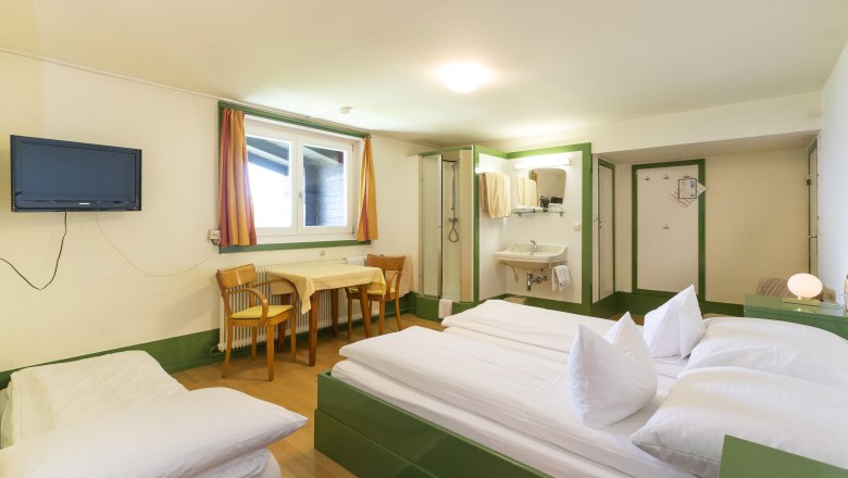 Looshaus, © Christian Redtenbacher A simply furnished hotel room with a double bed, table, chairs, TV and washing area.