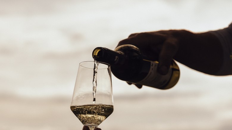 Pouring wine, © Weinviertel Tourismus / Sophie Menegaldo Wine is poured into a glass outdoors, with a landscape in the background.