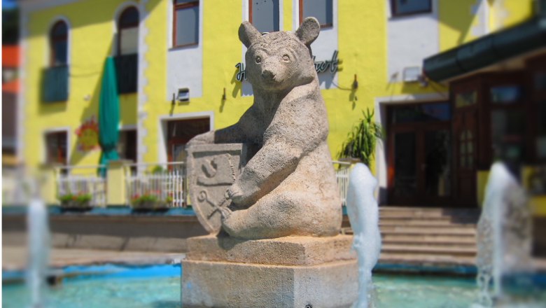Mats, © F. Brennig Stone bear sculpture with coat of arms in a fountain in front of a yellow building.
