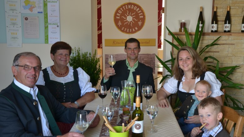 Krottendorfer family, © Familie Krottendorfer Family in traditional dress sitting at a table with wine and glasses.