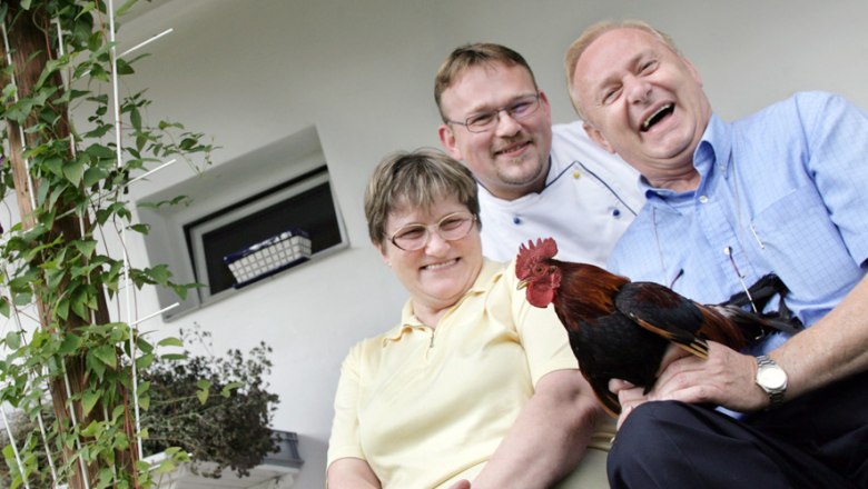 Bsteh family, © Franz Weingartner Three laughing people are sitting on a staircase, one is holding a rooster.