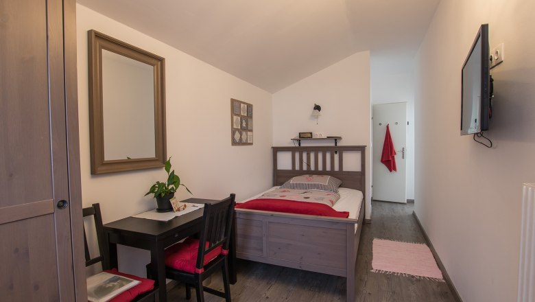 Double room Wolf, © A. Dirnbauer A cozy single room with wooden furniture, a bed, a small table with chairs, a mirror and a TV on the wall.