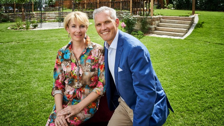 Kirchenwirt Wachau Manuela&Christian Wildeis, © Lehmann The Wildeis family are sitting in a meadow, smiling at the camera. The man is wearing a blue jacket, the woman a colorful dress.