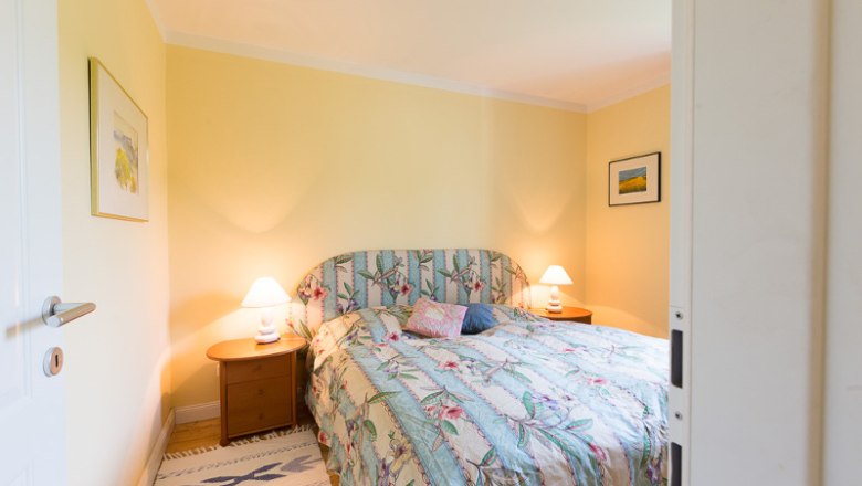 Bedroom, © Creative Design Cozy bedroom with double bed, floral comforter cover and two bedside tables with lamps. Yellow walls and pictures on the walls.