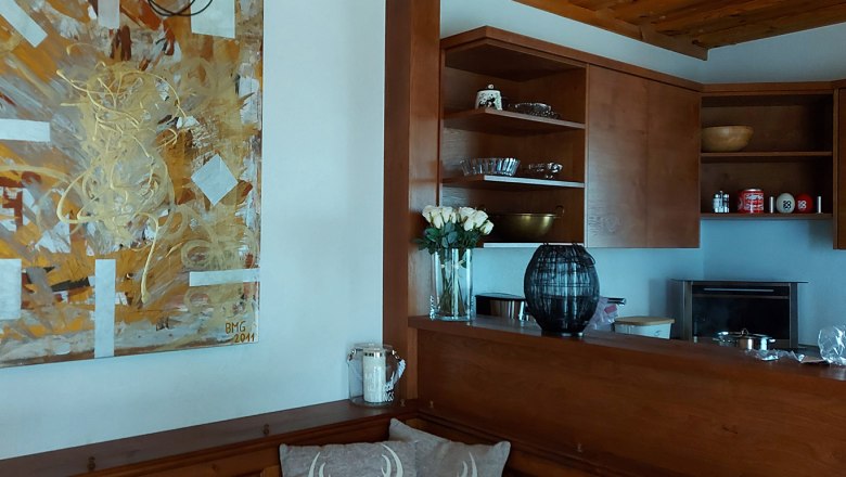 Kitchen, © Bernadette Gierlinger Wooden kitchen with artwork on the wall, vase with white roses and shelves with crockery.