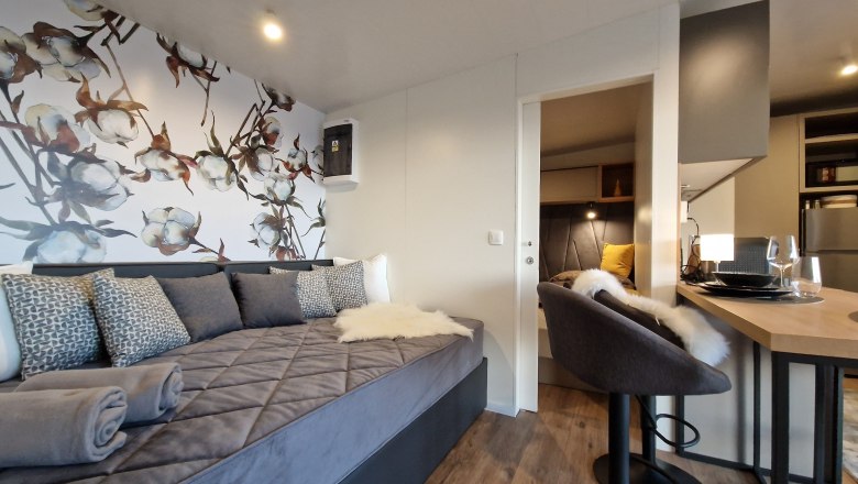 Couch Johannesbachklamm Chalet, © Johannesbachklamm Chalet Interior view of a modern chalet with gray sofa, decorative flower wall, bar stool and dining table.