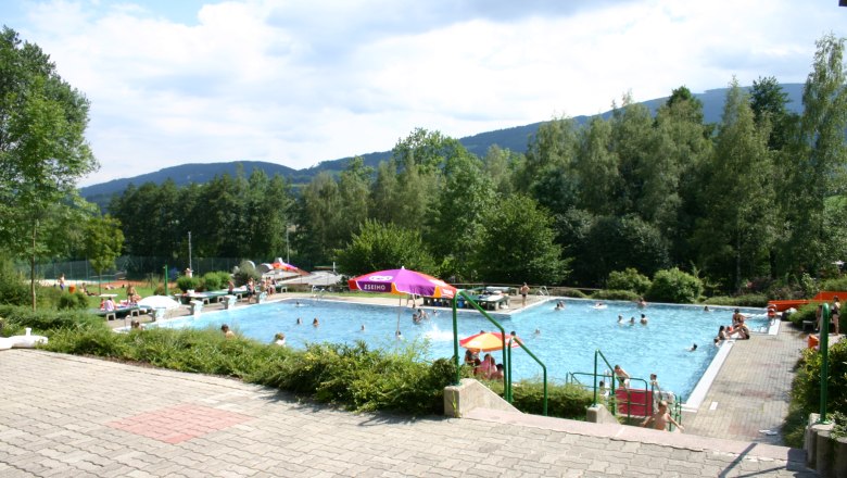 Kirchberg am Wechsel outdoor pool, © Steindy, CC BY-SA 2.0 DE Outdoor pool with floats and parasols, surrounded by trees and hills.