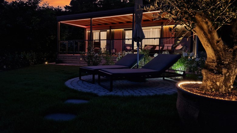 Exterior view of Johannesbachklamm Chalet., © Johannesbachklamm Chalet Exterior view of a chalet at sunset with sun loungers and illuminated tree in the foreground.