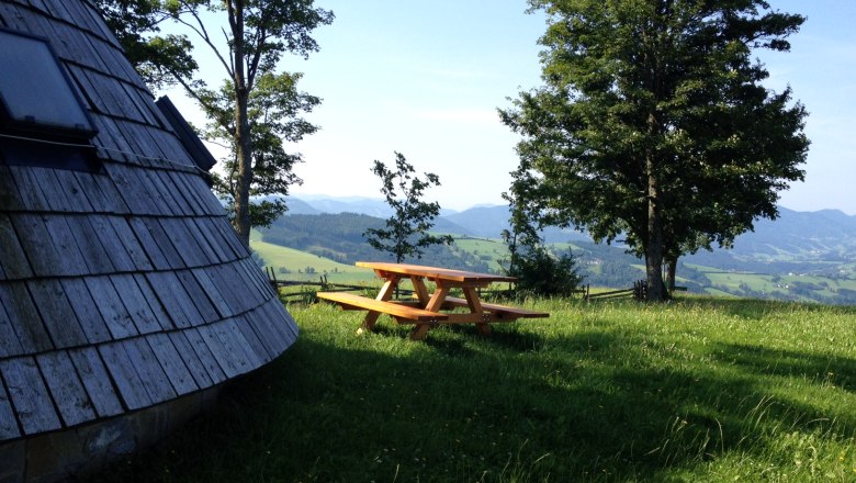 Sound garden, © Mostviertel Tourismus Wooden hut and picnic table on a meadow with trees and mountain views.