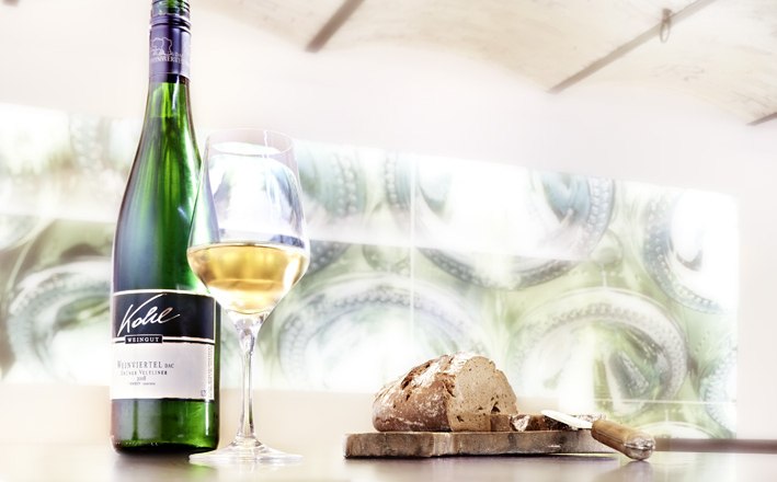 Kohl Winery, © Weingut Kohl A bottle of white wine, a filled wine glass and a loaf of bread on a table.