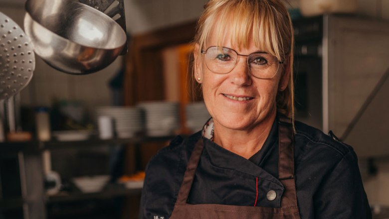 Landlady Ulrike Distelberger, © Niederösterreich Werbung/Daniela Führer A woman in chef's clothes stands in a kitchen and smiles at the camera.