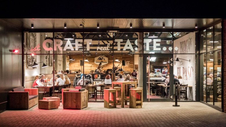 Ignition unit, © Lukas Kirchgasser Photography Exterior view of a restaurant with a glass front, inside people are sitting at tables.