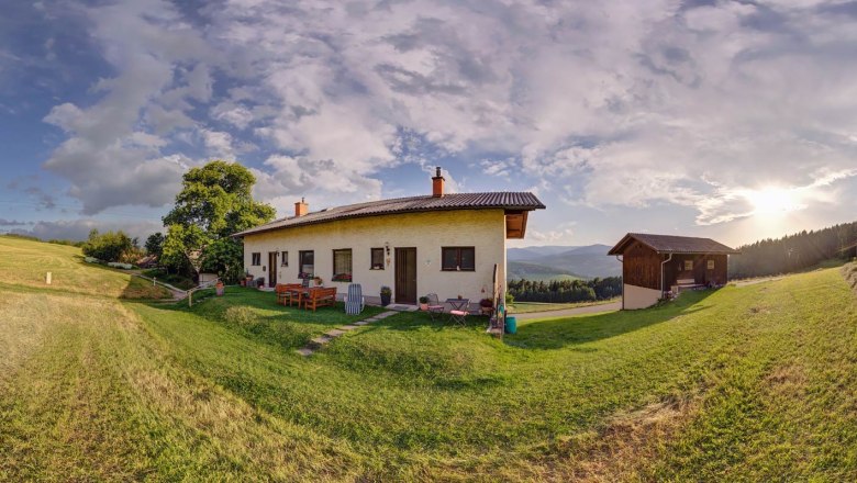 Wachahof Panorama, © Wachahof Panoramic view of a house on a meadow with trees and mountains in the background at sunset.