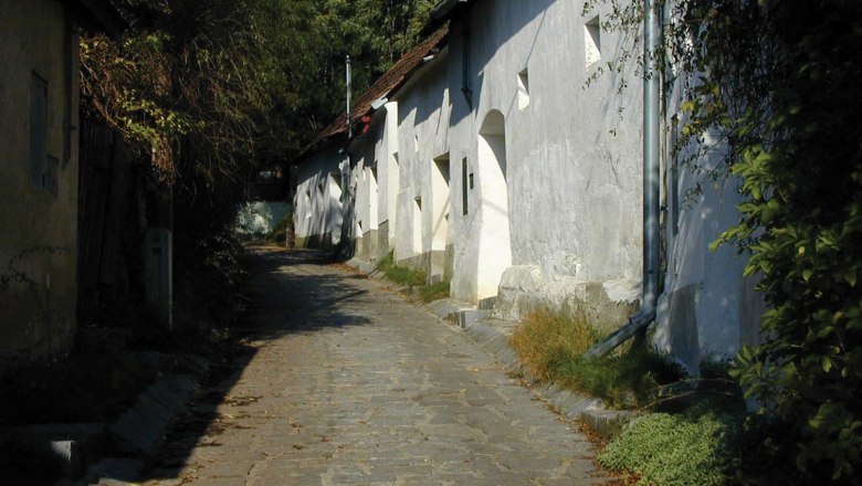 Enzersfeld wine cellar lane, © Gemeinde Enzersfeld A narrow, cobbled lane with white buildings and green vegetation in Enzersfeld.