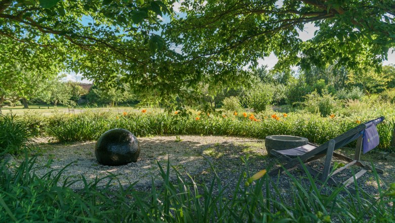 Altenburg Abbey, © Martina Draper A garden with a black ball, a deckchair and blossoming flowers under a tree.