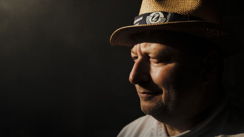 Barbecue world champion Adi Bittermann, © Niederösterreich Werbung/Michael Reidinger Portrait of a man with a straw hat in profile, standing in the shade.