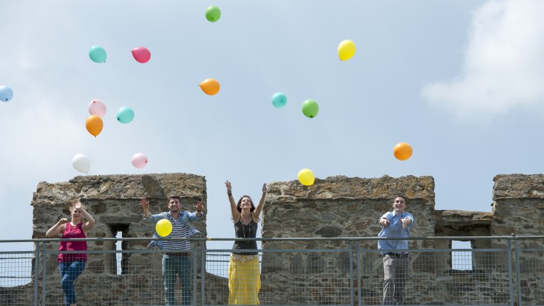 Battlement hike, © M. Himml Four people throw colorful balloons into the air from a castle wall.