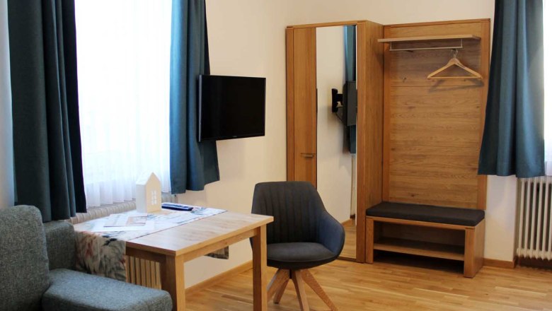 Guest room, © Magdalena Donhauser Modern guest room with table, chair, closet, sofa, TV and blue curtains.