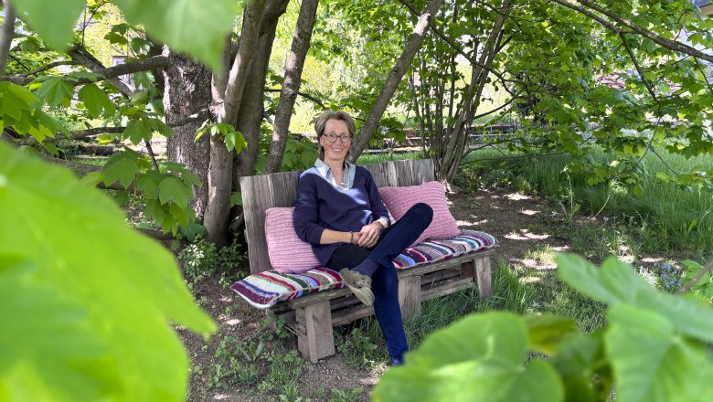 Gitti's garden paradise, © "Natur im Garten" A person is sitting on a bench in the garden, surrounded by green leaves and trees.