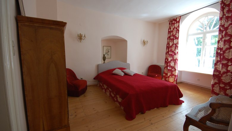 Seminar house DIE LICHTUNG, © Seminarhaus DIE LICHTUNG A cozy bedroom with a red bed, red curtains and wooden furniture.