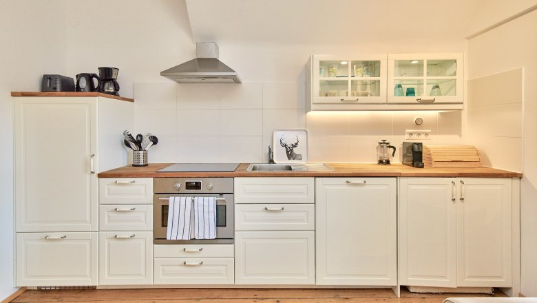 Top 7 - Kitchen, © VP FeWo OG Modern kitchen with white cupboards, wooden worktop, stove, extractor hood and sink.