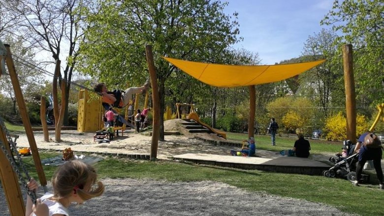 KremsStein playground, © Roman Zöchlinger Children play on a playground with swings and climbing frames under a yellow awning.