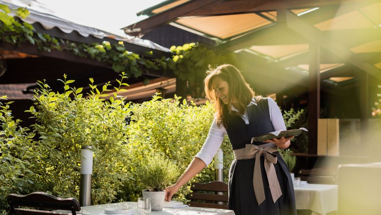 Garden at Landgasthaus Essl, © Inge Funke A woman in traditional dress prepares a table in the garden of a country inn.