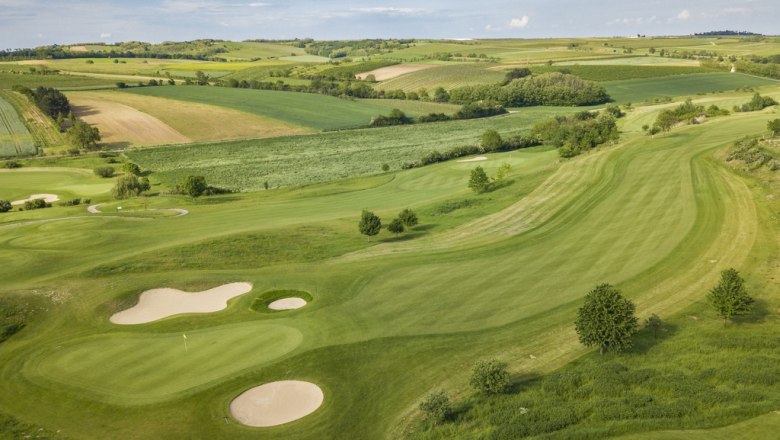 Poysdorf Golf Club, © Golfclub Poysdorf Aerial view of a golf course with green fairways and sand bunkers, surrounded by fields and hills.