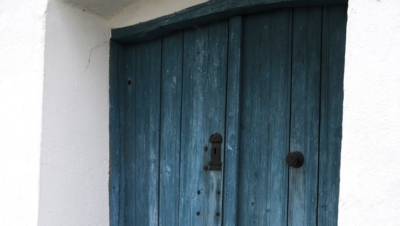 Cellar door, © Weinviertel Tourismus / Mandl Blue wooden door in a white building with cobblestones in front of it.